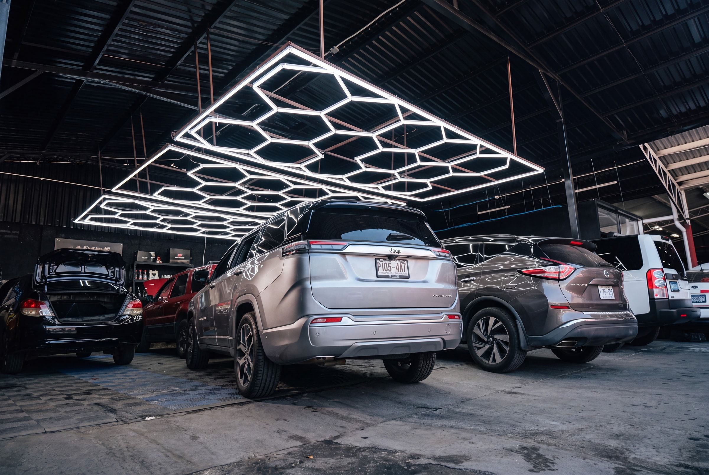 Nave de trabajo del taller Smartfix en Santa Tecla, iluminada por una parrilla hexagonal de LED, con vehículos modernos sobre piso limpio